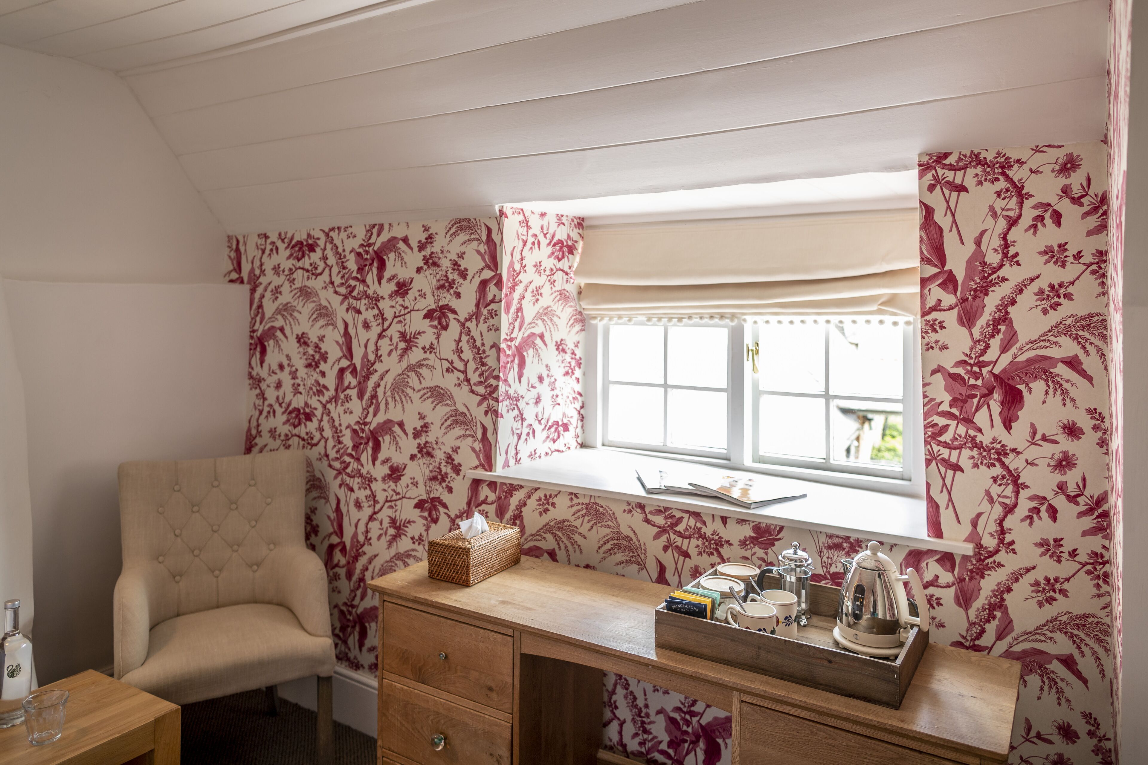 Una habitación acogedora con un escritorio de madera, una silla acolchada, una ventana con cortinas florales y vistas al exterior.