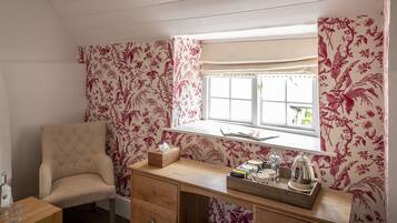 Una habitación acogedora con un escritorio de madera, una silla acolchada, una ventana con cortinas florales y vistas al exterior.