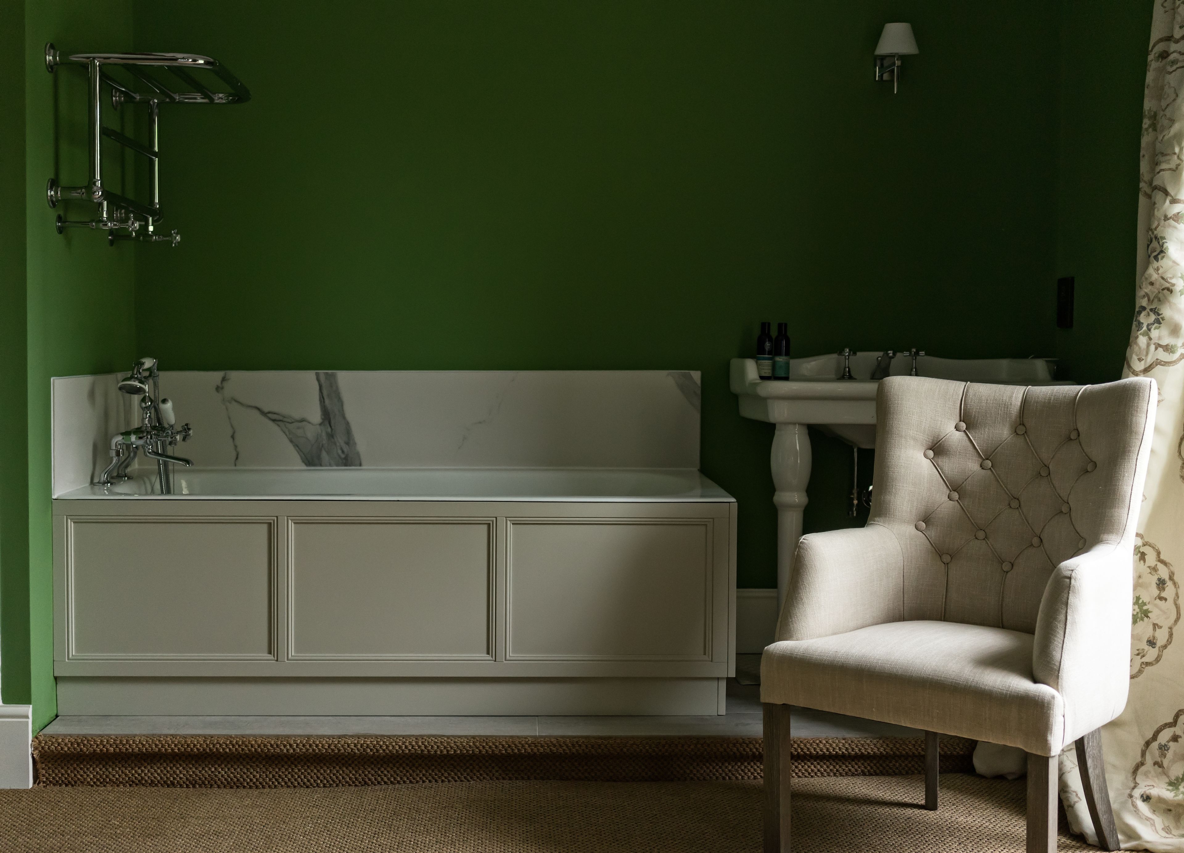 A bathroom with a white bathtub, a green wall, a white sink, and a chair.