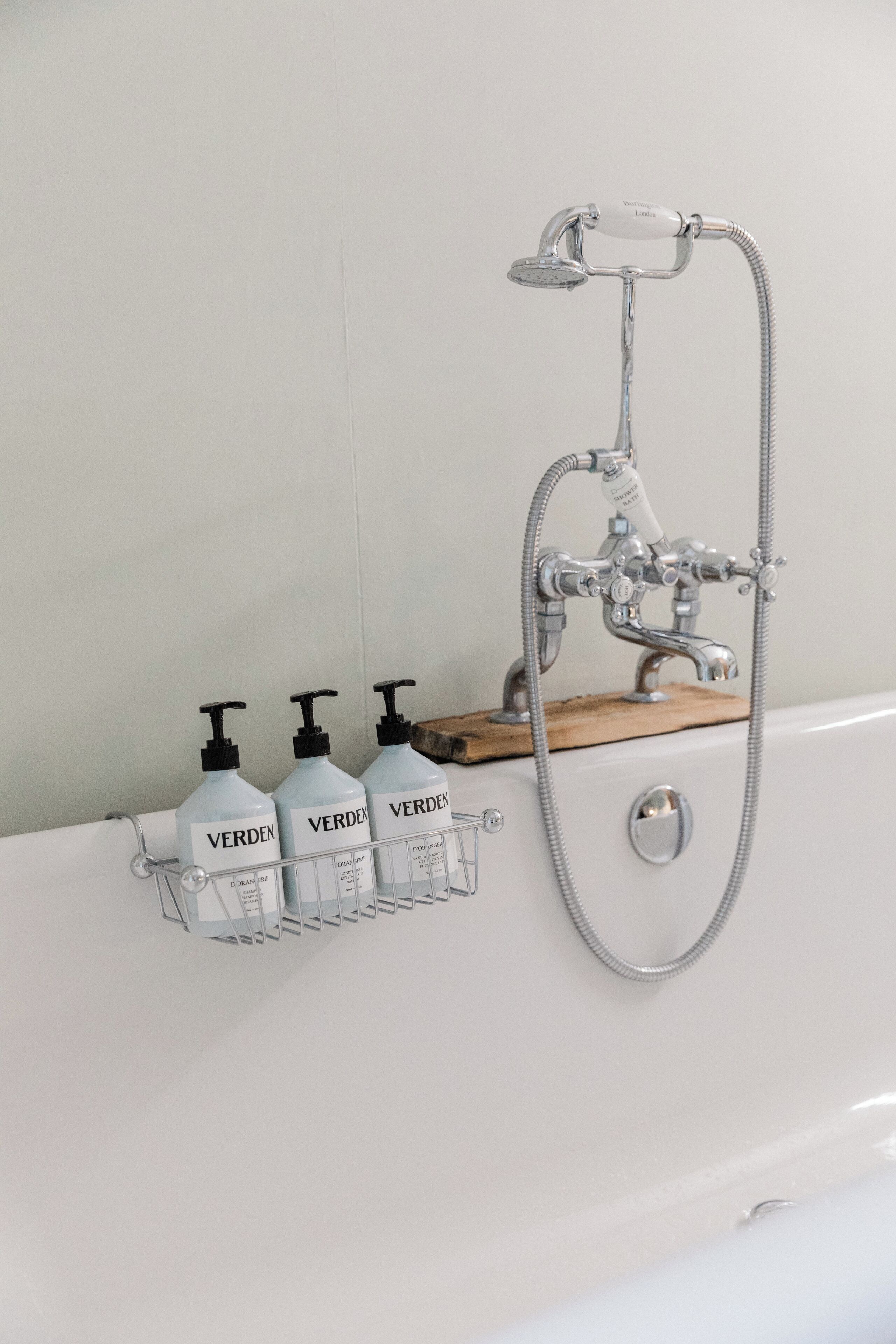 A bathroom with a bathtub, a shower, and a soap dispenser holder with three bottles.