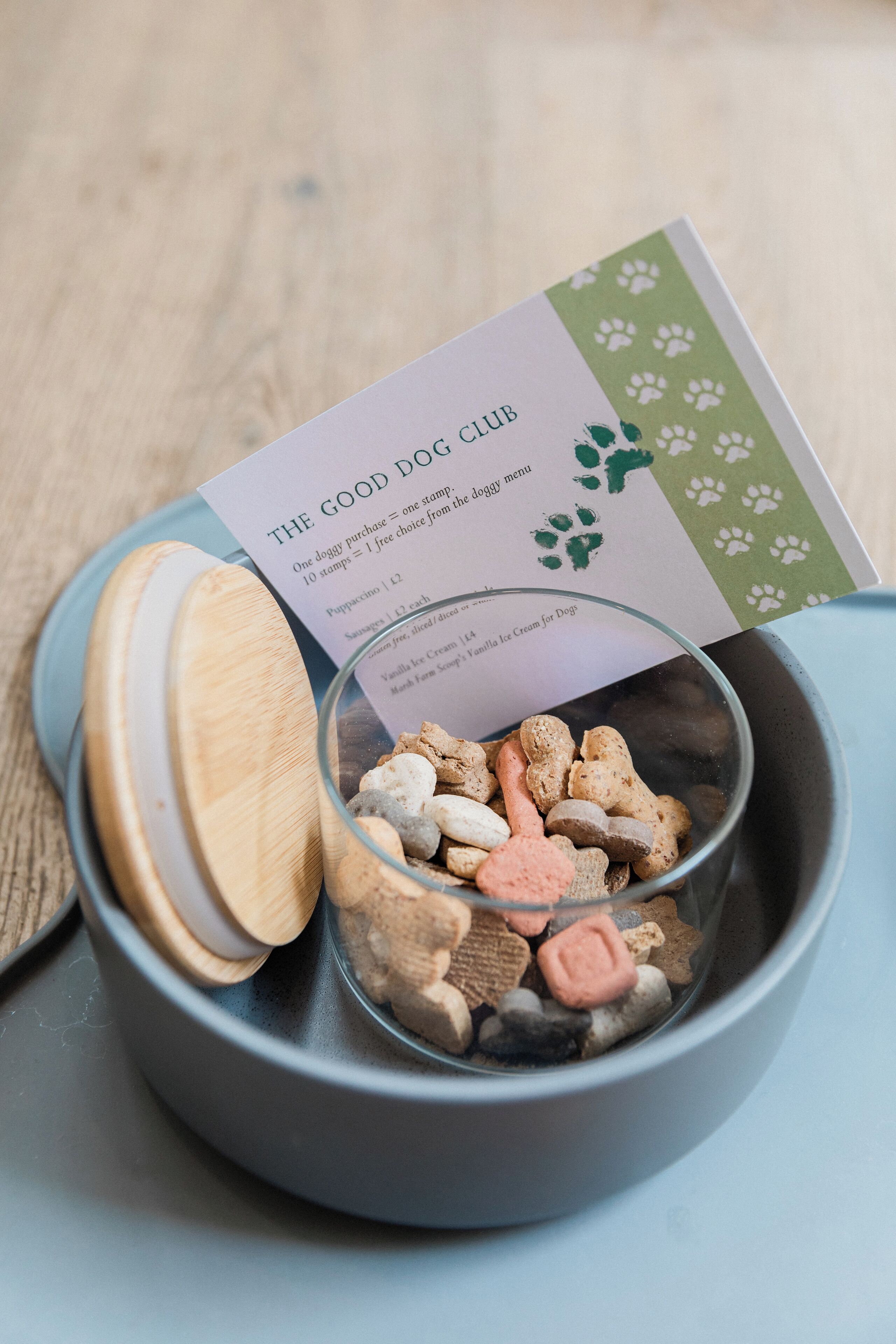 A bowl of dog treats with a card and a wooden lid.