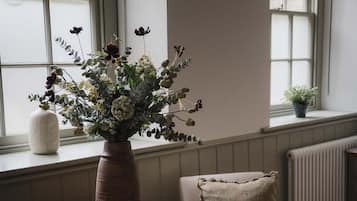 A room with a round wooden table, a chair, a vase with flowers, and a window with a view of trees.