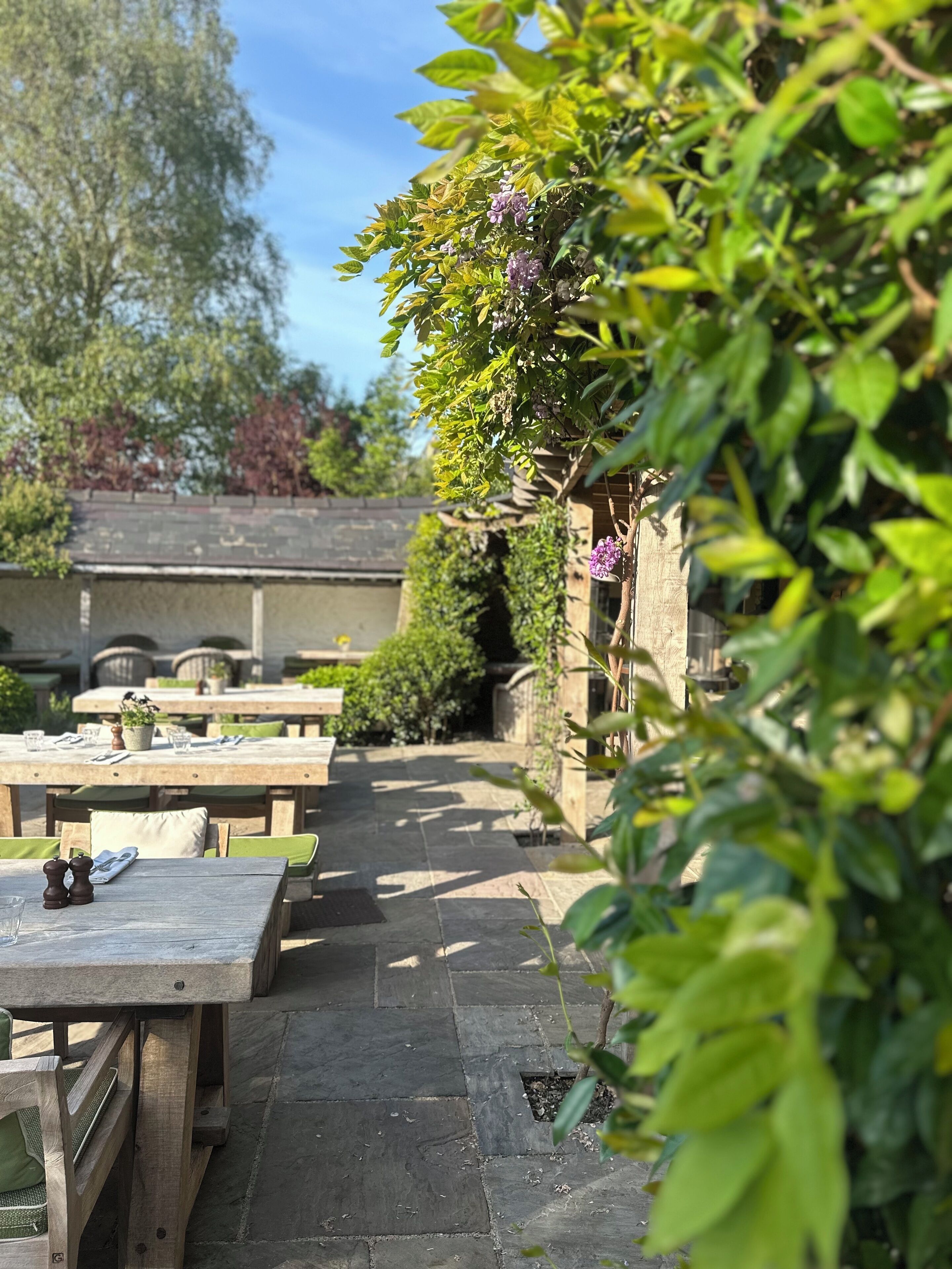 An outdoor patio with stone flooring, wooden tables, and chairs.