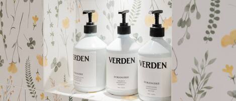 Three bottles of Verden body wash on a shelf against a floral wallpaper background.
