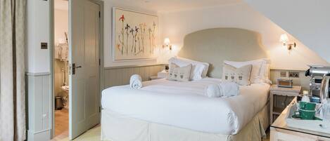 A neatly arranged bedroom with a large bed, a bedside table, a nightstand, and a wall-mounted lamp.