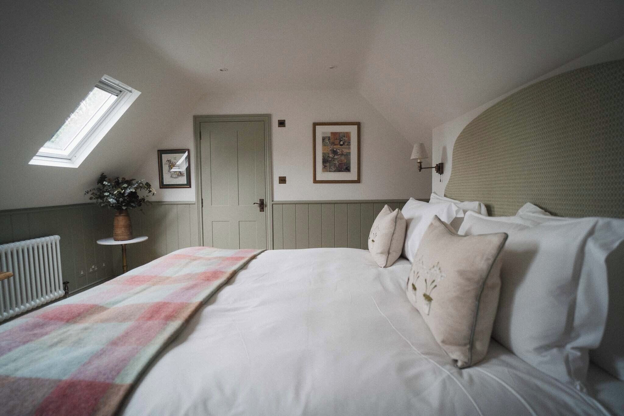 Un dormitorio con una cama grande, una mesita con una planta, una puerta y una ventana.