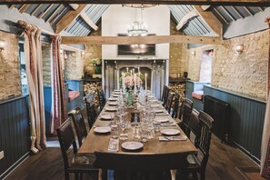 A long dining table set for a meal in a rustic room with stone walls and wooden beams. - The Swan Inn (Chipping Norton)