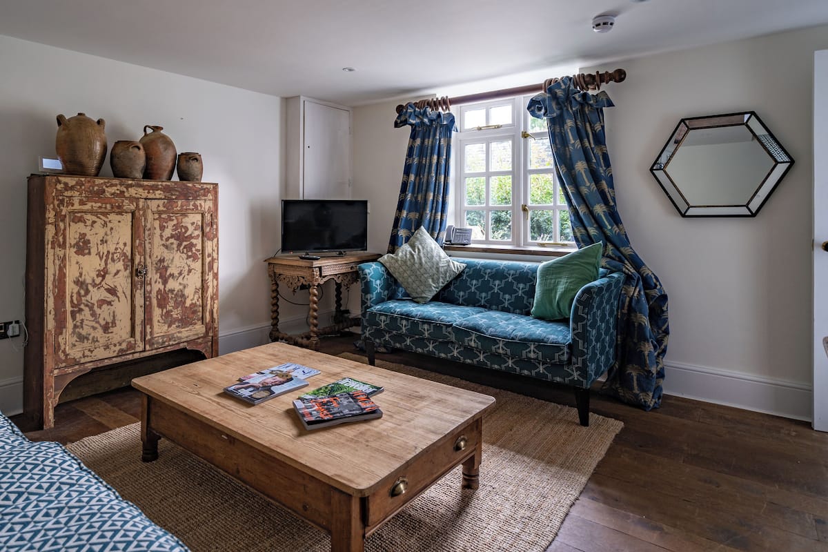 A living room with a wooden coffee table, a blue patterned sofa, a wooden cabinet, and a television.