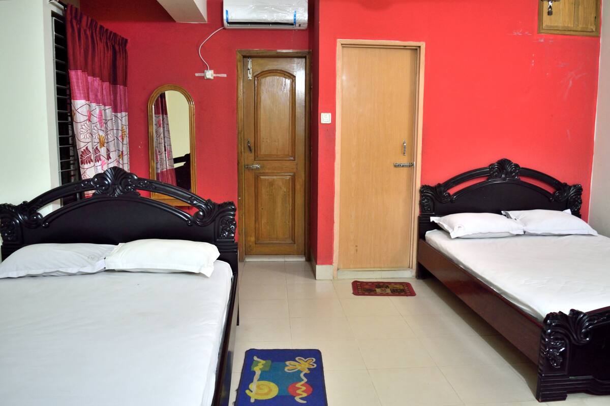 A bedroom with two beds, a wooden door, a mirror, and a red wall.