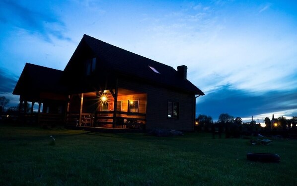Situated in a serene rural setting, this cabin features a spacious porch and a large window on the upper floor.