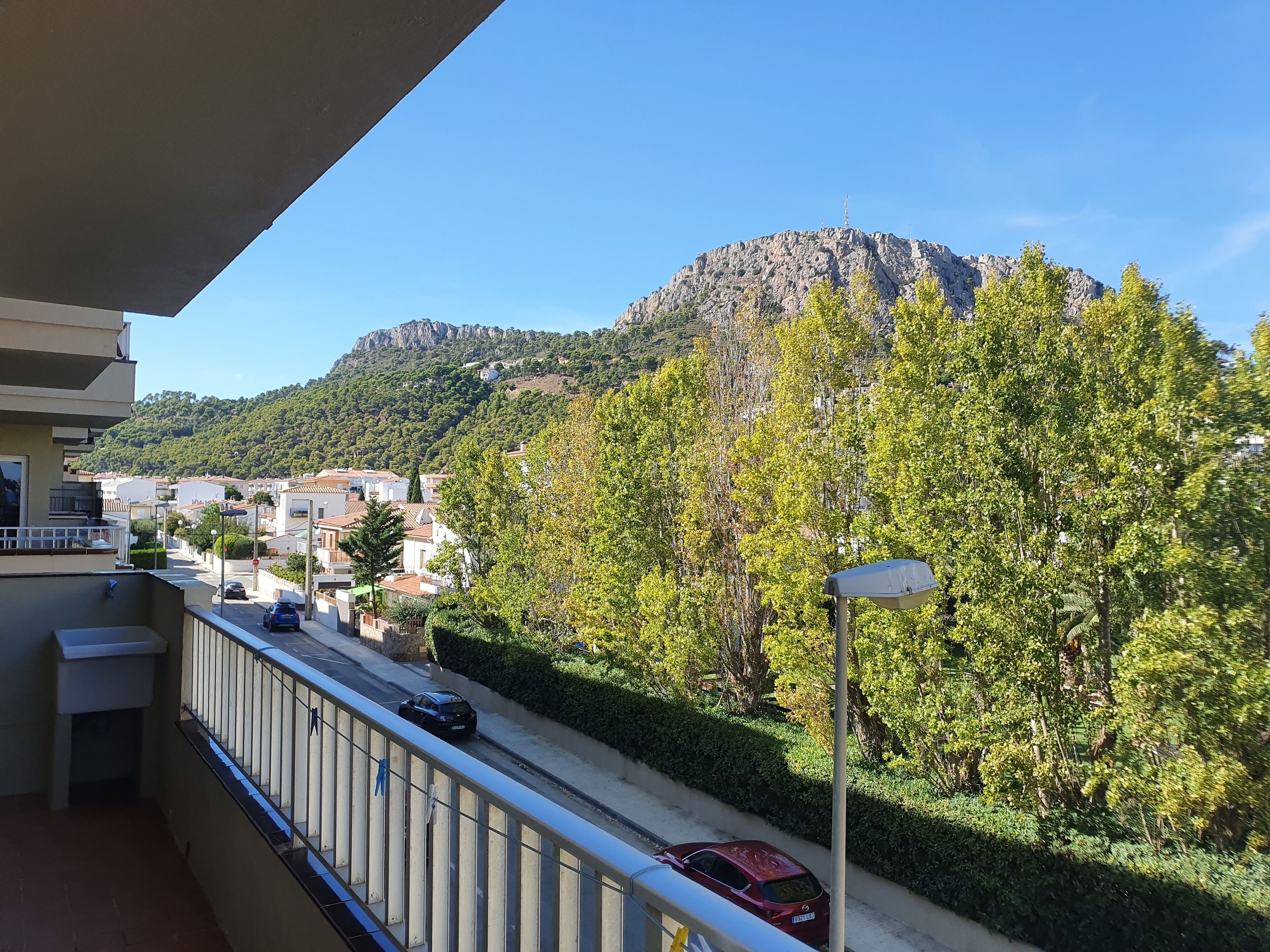 Un balcón con vistas a una calle, coches y una montaña.