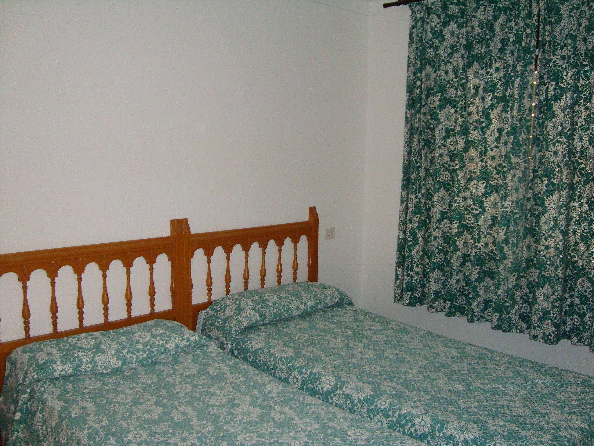 A room with a wooden bed frame and floral-patterned bedding.