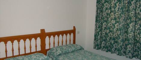 A room with a wooden bed frame and floral-patterned bedding.