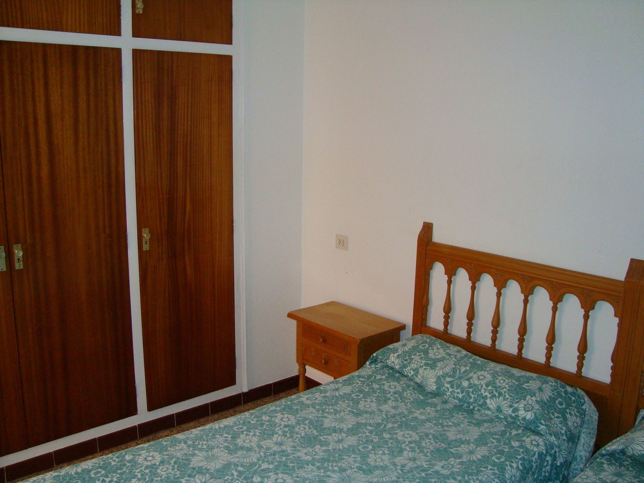 Un dormitorio con una cama de madera, una mesita de noche y un armario.