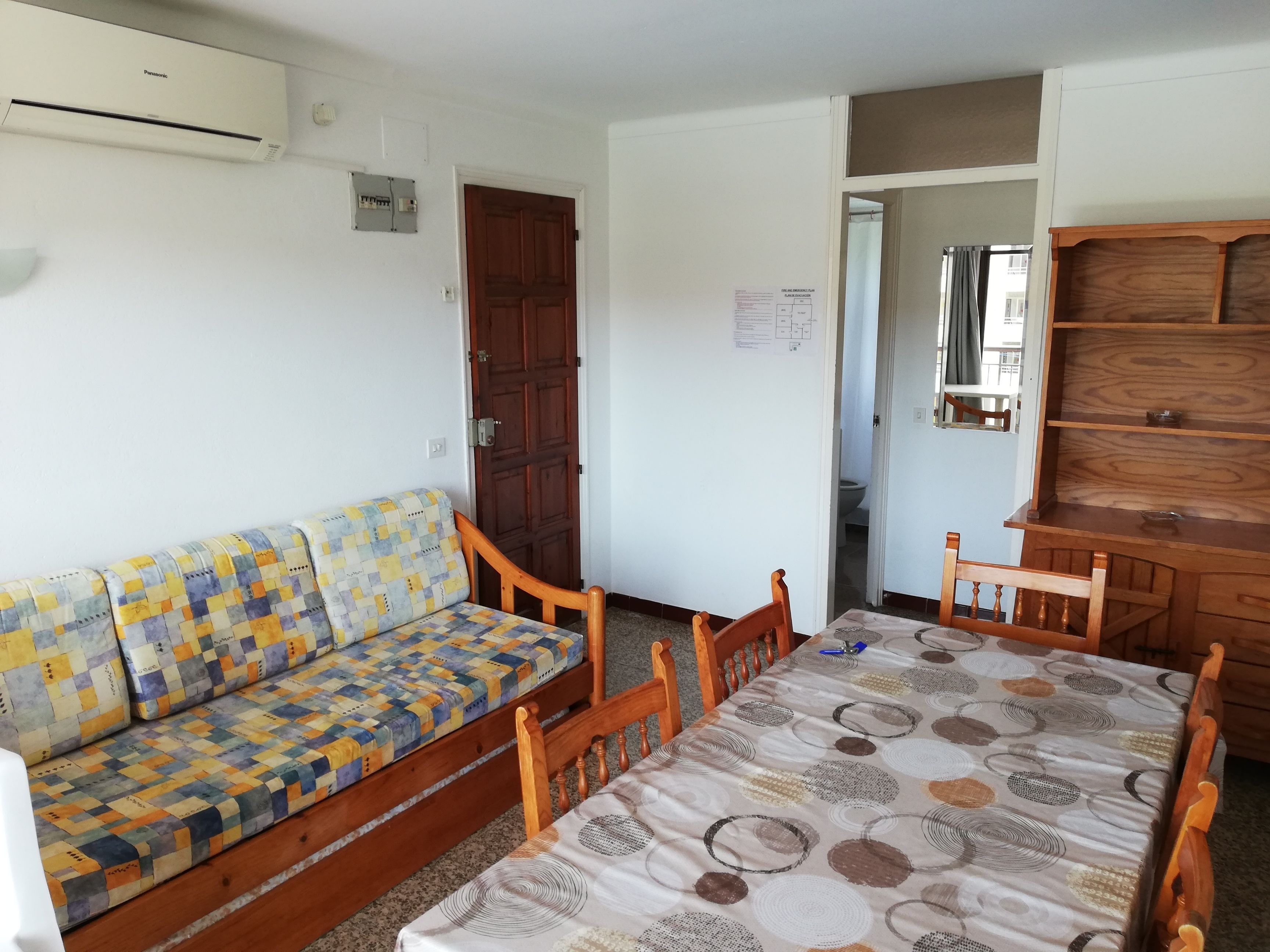 A room with a wooden sofa, a wooden dining table, a wooden cabinet, and a door leading to a bathroom.