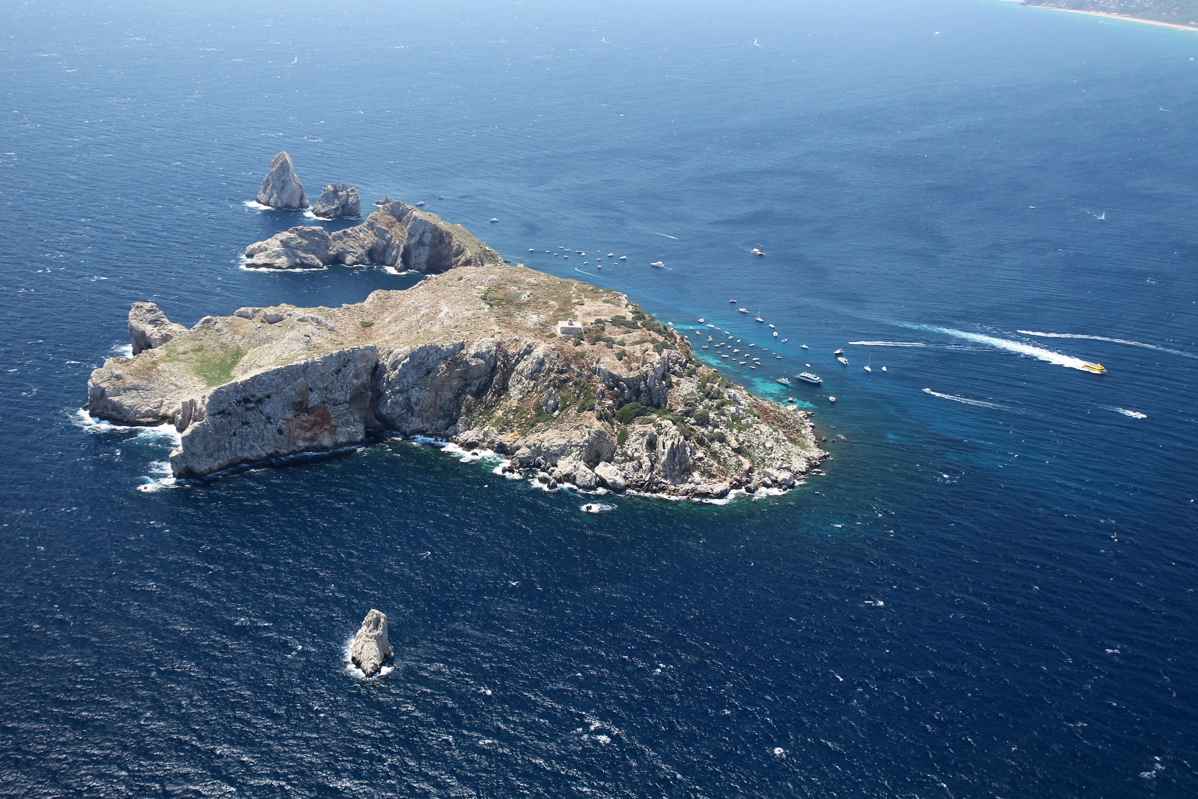 An aerial view of a rocky island with clear blue waters and boats.