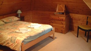 A wooden cabin room with a bed, a dresser, a chair, and a lamp.