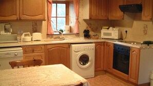 A compact kitchen with wooden cabinets, a washing machine, a microwave, and a stove.
