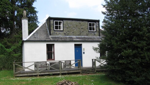 A two-story house with a blue door, a chimney, and a wooden deck leading to the front door.