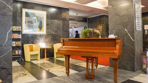 A lobby with a grand piano, a checkered floor, a framed artwork, and a sign indicating room numbers.