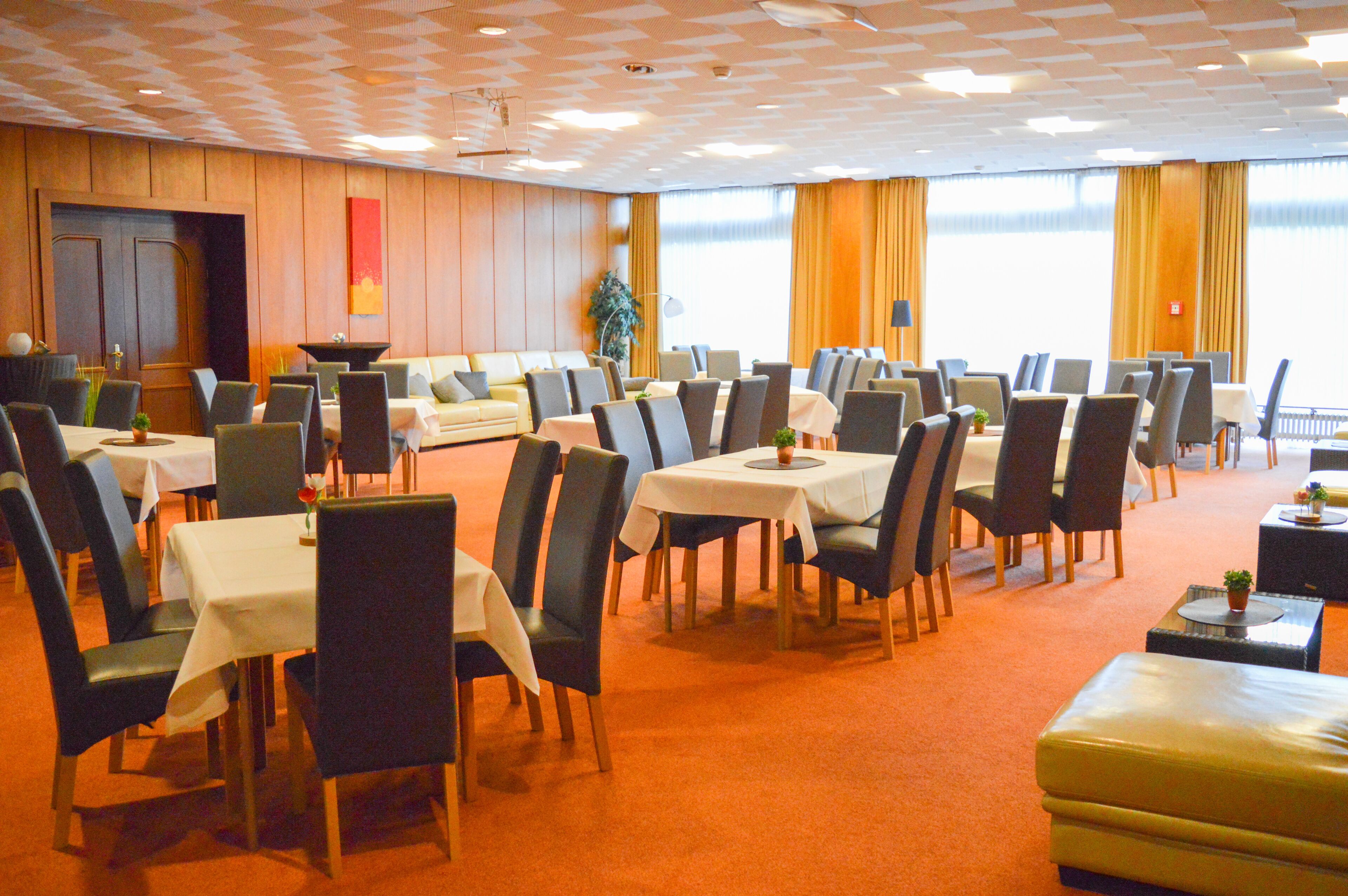 Ein Hotel-Essbereich mit mehreren Tischen und Stühlen, einer Couch und einem großen Fenster mit Vorhängen.