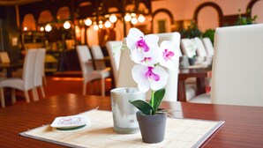 A dining table with a potted orchid, a candle, and a placemat in a restaurant setting.