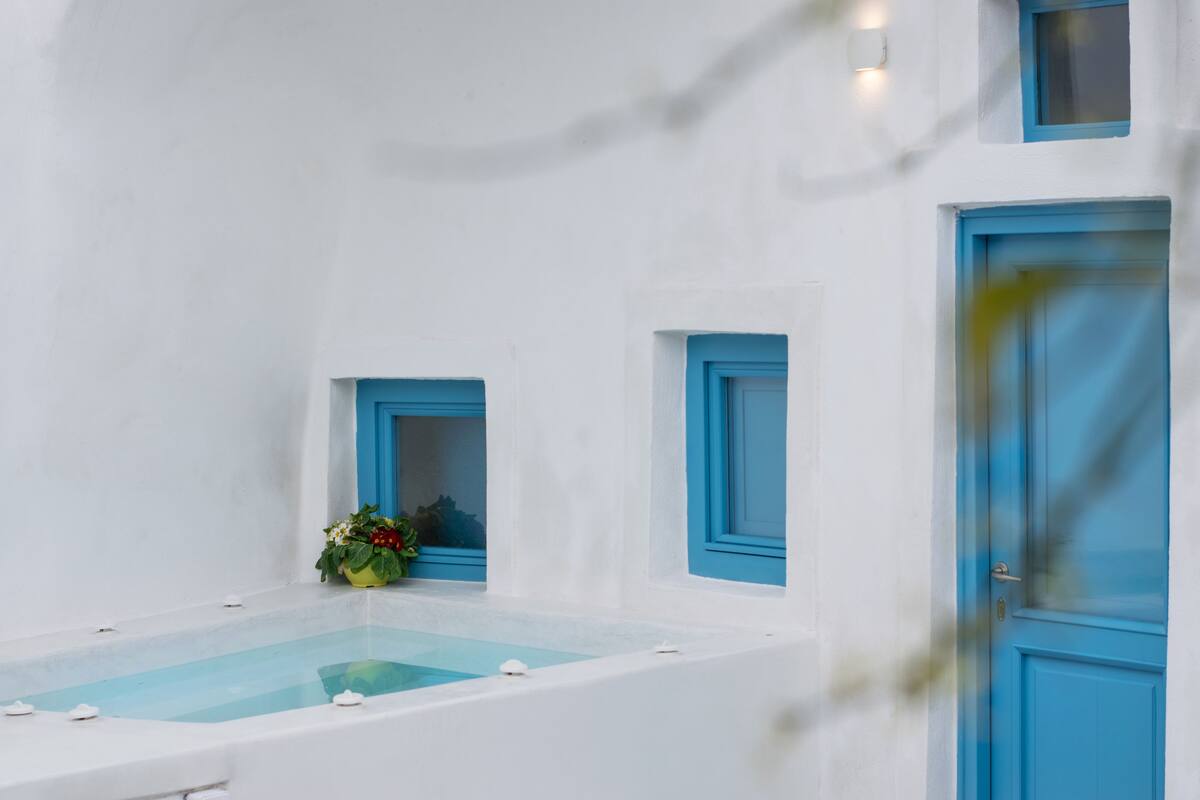 Una habitación blanca con una bañera, una puerta azul y un ventanal con detalles azules.