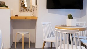 A modern room with a round dining table, white chairs, a mounted TV, and a unique hexagonal floor design. - Stoa Cave Villas (Santorini)