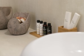 Une salle de bain avec un lavabo blanc, un tapis de bain en bois et trois bouteilles de produits pour les soins capillaires.