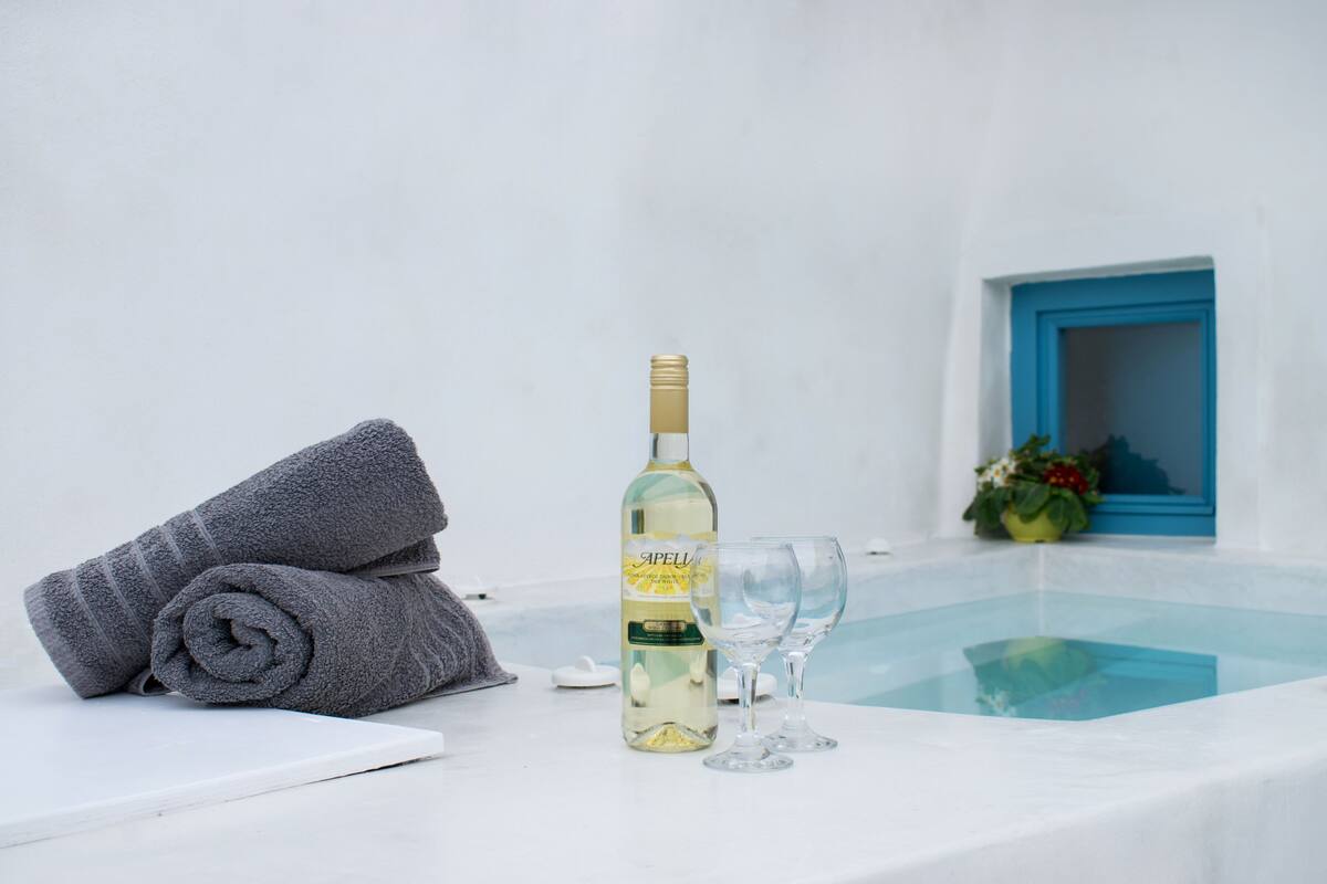 Habitación blanca con una botella de vino Apell, dos copas y una toalla enrollada.