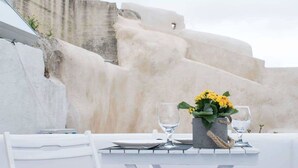 A table set with a vase of yellow flowers, two glasses, and a white tablecloth against a backdrop of a stone wall. - Stoa Cave Villas (Santorini)