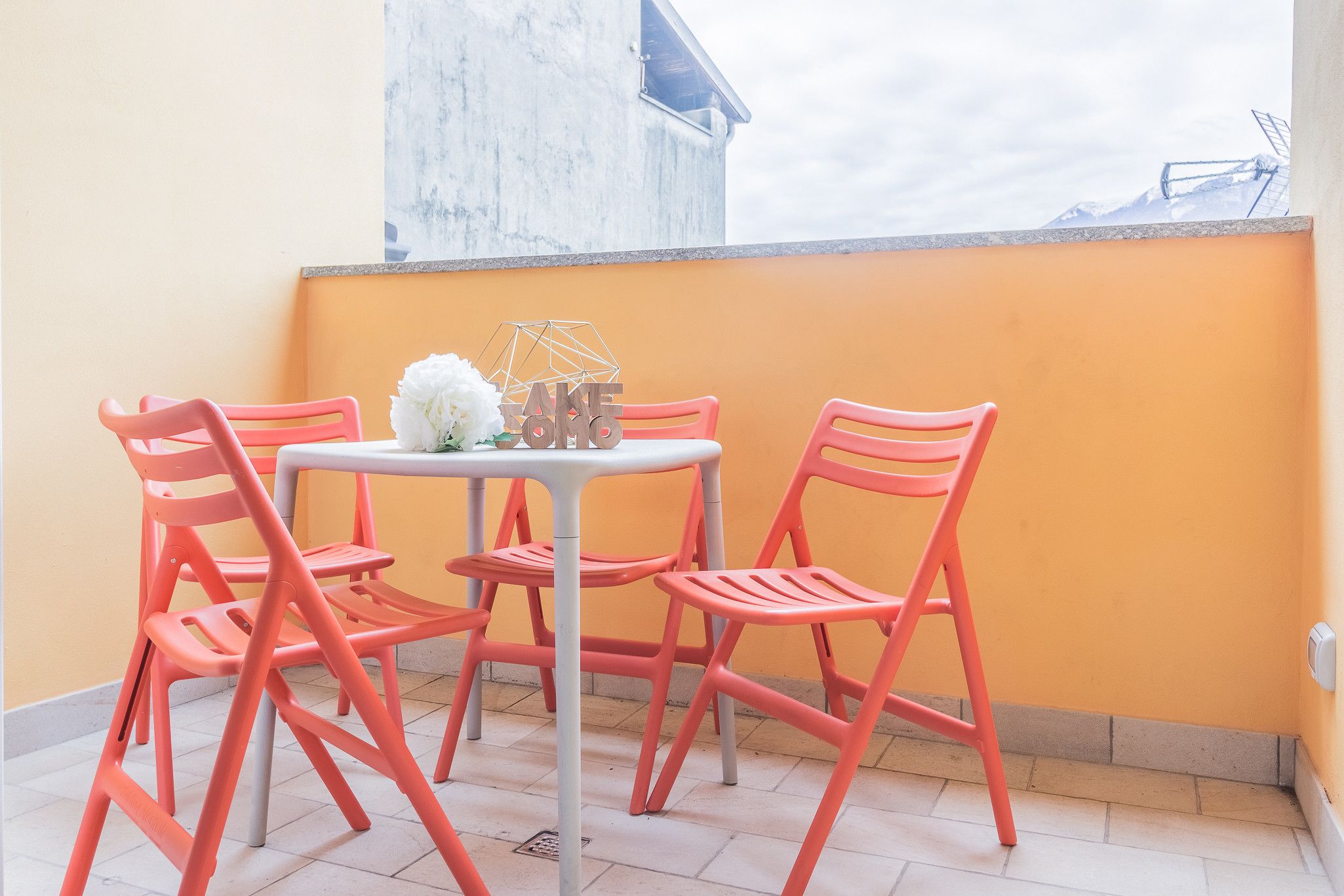 A small outdoor seating area with a table and four chairs, a white flower arrangement, and a view of a mountain in the background.
