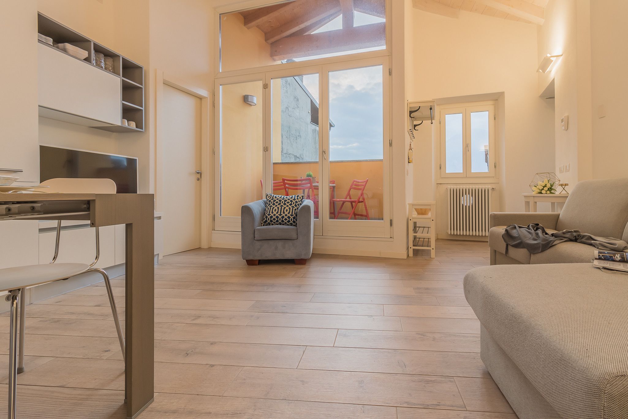 Una habitación amplia con un gran ventanal corredero que da a un espacio exterior, un sofá, una pequeña mesa y una silla.