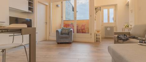 Una habitación amplia con un gran ventanal corredero que da a un espacio exterior, un sofá, una pequeña mesa y una silla.