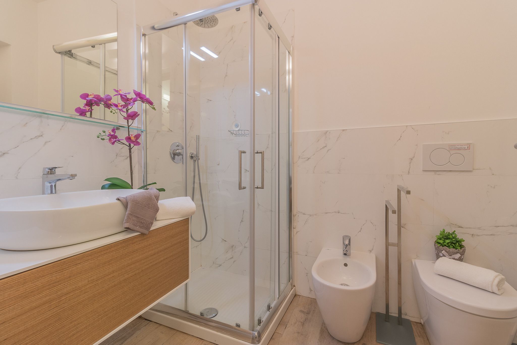Un baño moderno con ducha envuelta en vidrio, lavamanos, bidé e inodoro.
