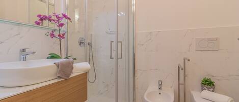 Un baño moderno con ducha envuelta en vidrio, lavamanos, bidé e inodoro.