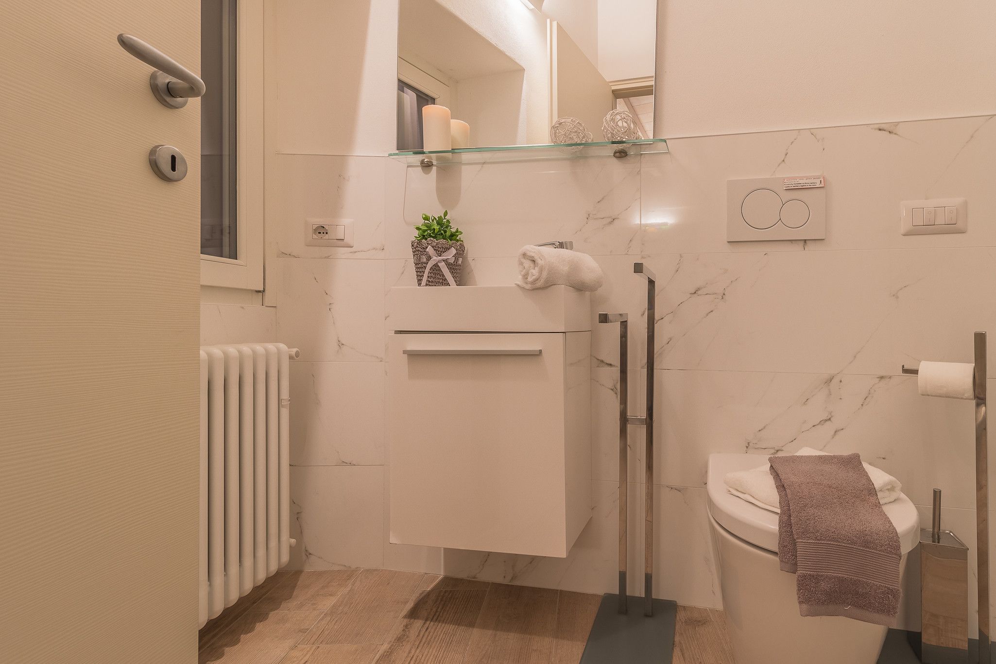 A modern bathroom with a glass shelf, a towel rack, a toilet, and a radiator.
