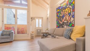 A living room with a sofa, a chair, and a table. There is a large window and a door leading to an outdoor area. - Casa Manoli Varenna (Varenna)
