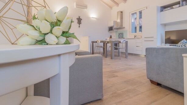 A modern living room with a grey sofa, a dining table, and a kitchen area in the background. - Casa Manoli Varenna (Varenna)
