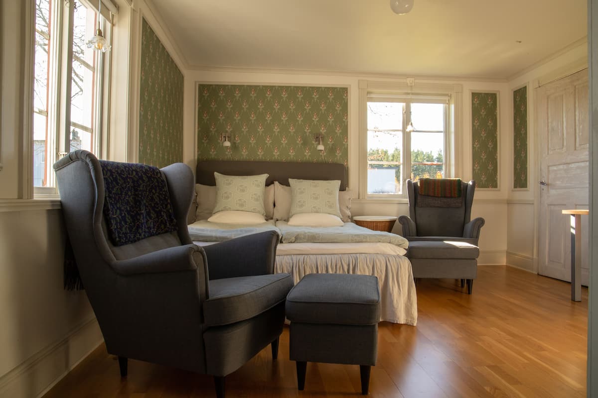 Une chambre à coucher avec un lit, deux fauteuils, une petite table et une fenêtre donnant sur un beau paysage.