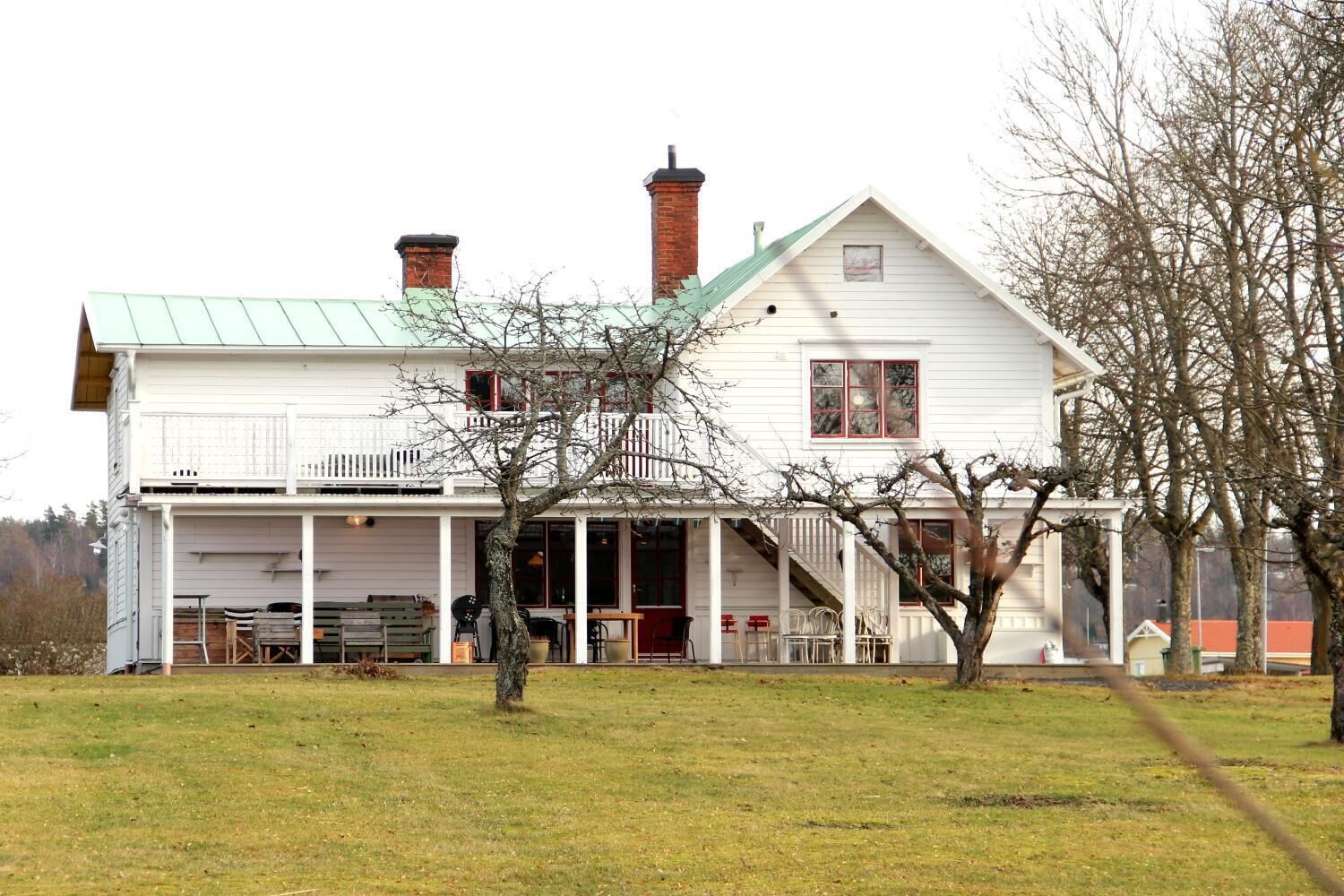 Una casa blanca de dos pisos con techo verde, un porche cubierto y un patio cercado.