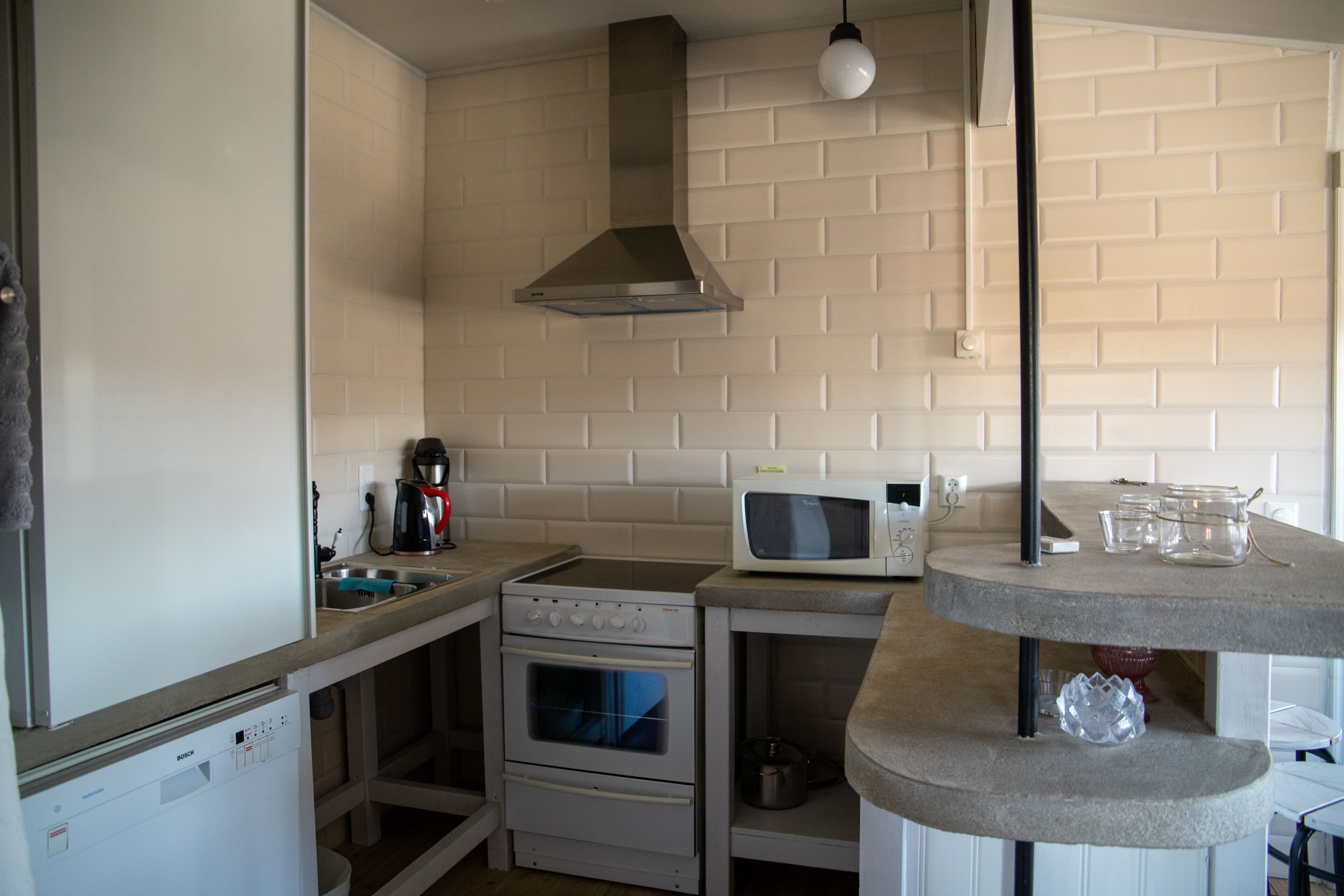 A compact kitchen with a dishwasher, stove, oven, microwave, and a hanging light fixture.