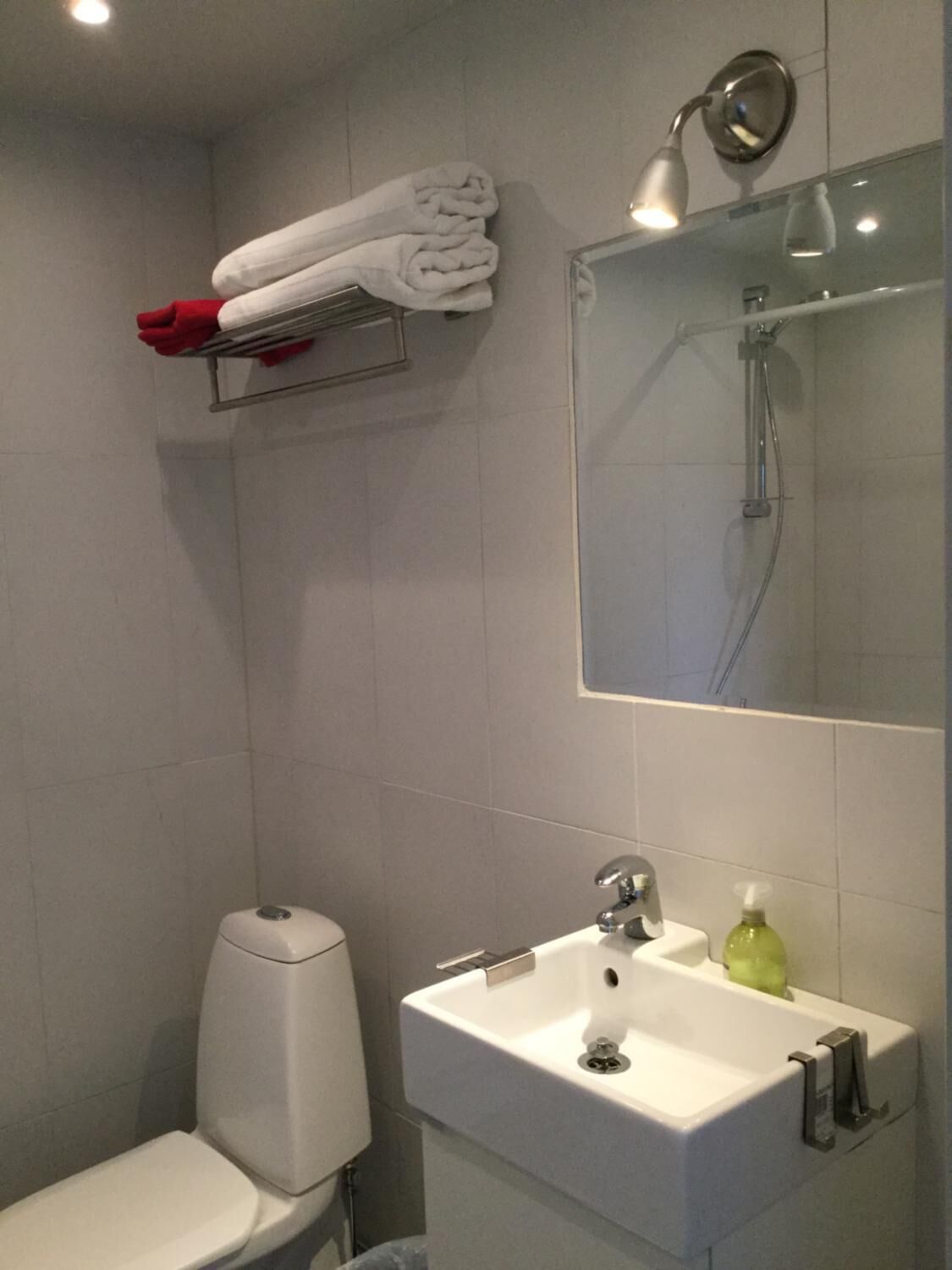 Un baño con inodoro, lavamanos y espejo. Toallas apiladas en un estante sobre el espejo.
