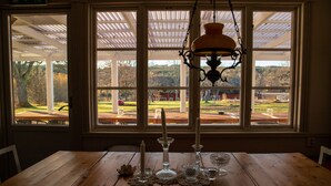 A wooden table with candles and glassware, a hanging lamp, and a view of a park through large windows.