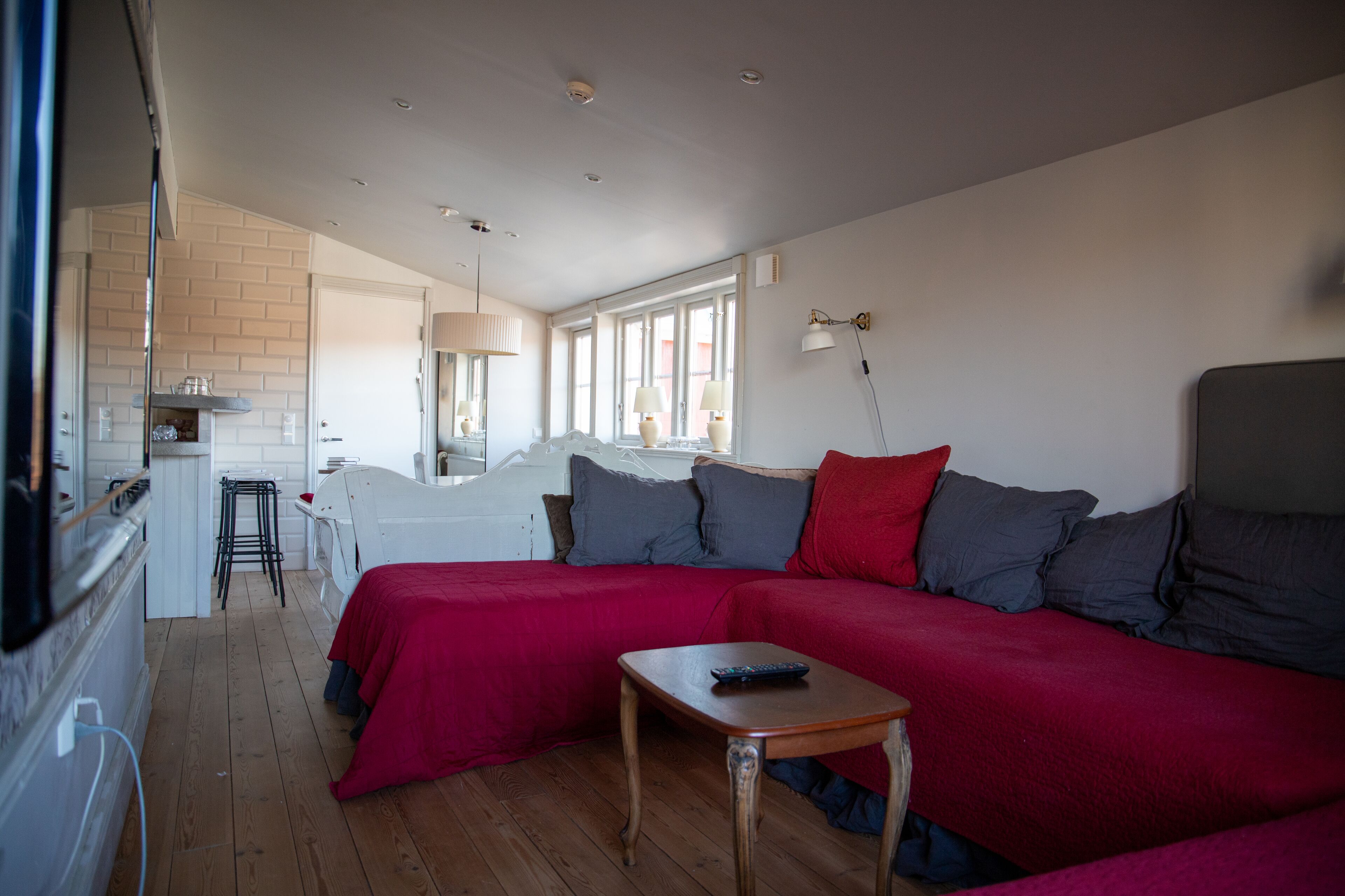 Un salón acogedor con un sofá rojo, una mesita de madera y una zona de cocina al fondo.