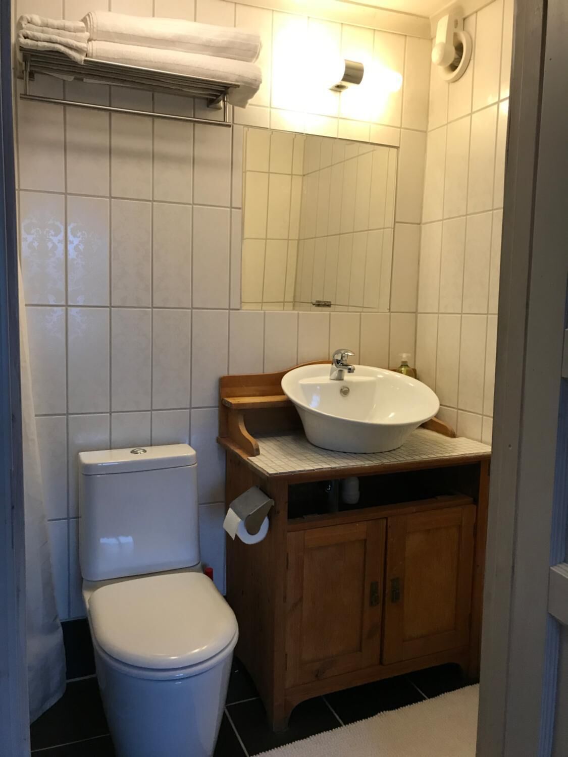 Un baño con inodoro blanco, tocador de madera con lavamanos y espejo sobre el tocador.