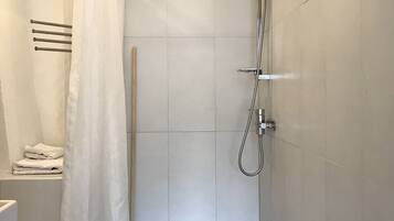 A small, modern bathroom with a shower, toilet, and a towel rack.