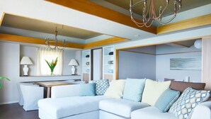 A modern living room with a sectional sofa, a glass coffee table, and a chandelier. - Winbell Okinawa Nago Coral View (Nago)