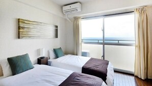 A hotel room with two beds, a large window with a view of the sea, an air conditioning unit, and a painting on the wall. - Winbell Okinawa Nago Coral View (Nago)