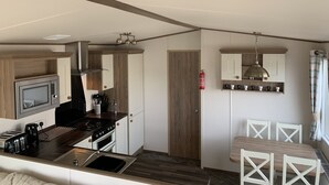 Cocina compacta con microondas, estufa y pileta, muebles de madera y comedor con mesa y sillas.